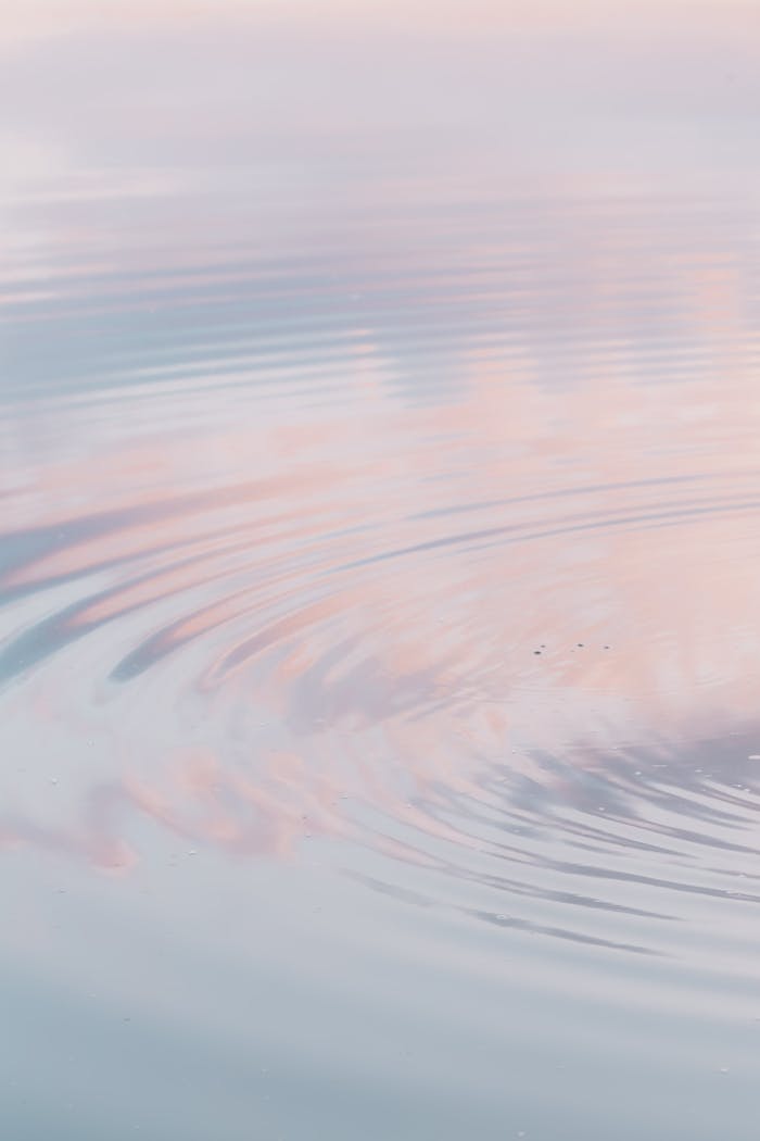 Peaceful ocean ripples reflect a pastel sky at sunset, creating a tranquil scene.